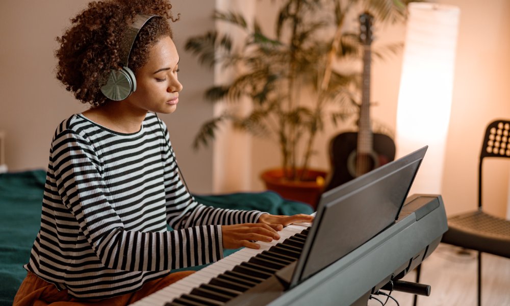 A young woman wearing headphones closing her eyes as she plays notes on an electronic keyboard.