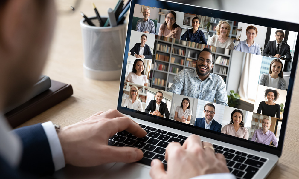 A remote employee sitting at a desk with his laptop open. The screen shows a team meeting with several boxes.