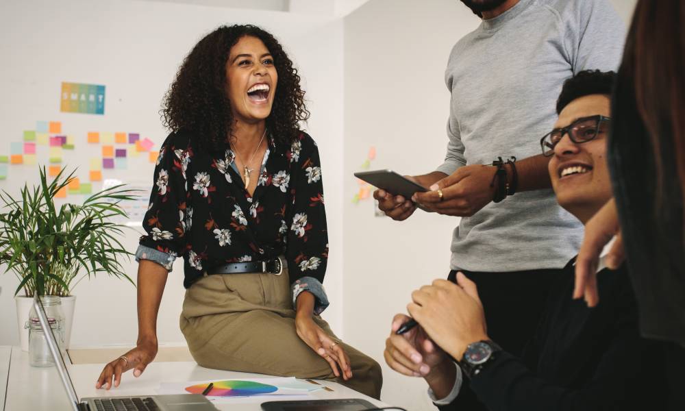 A group of business colleagues gathered around a white work table, laughing and smiling together.