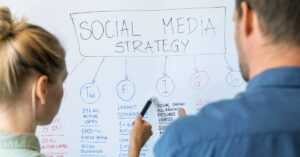 Two coworkers standing shoulder-to-shoulder and analyzing a whiteboard that reads “social media strategy.”