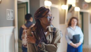 A teenage girl holds her arm as she walks through a school hallway. She looks upset and withdrawn.