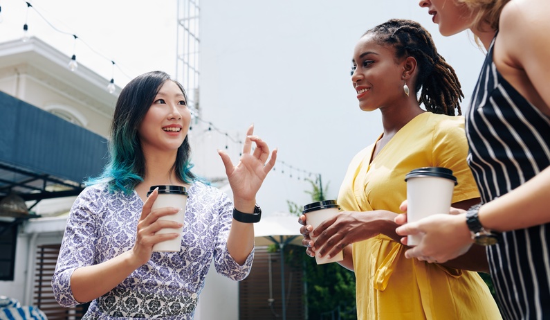A trio of fashionable, diverse coworkers gathered outside to have a friendly conversation over coffee.