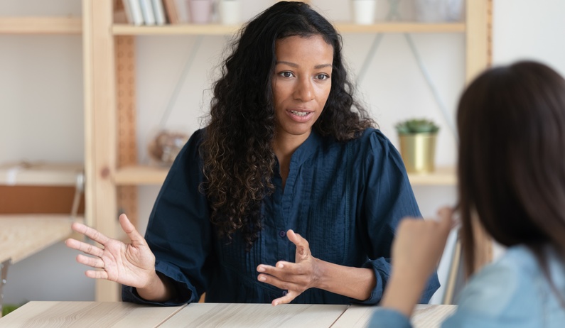 An employee sitting across from a member of their HR department and having a confident, calm conversation while gesturing.