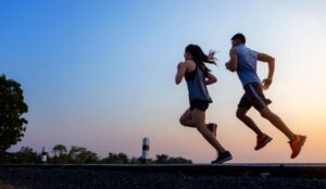 A silhouetted woman and man run on a path at sunrise, with a gradient sky of blue and orange in the background.