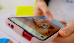A person scrolling their social media feed while sitting at a table with printed professional documents on it, including graphs and charts.