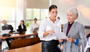 A pair of coworkers reviewing paperwork together in a boardroom. One worker is young, and the other is mature.